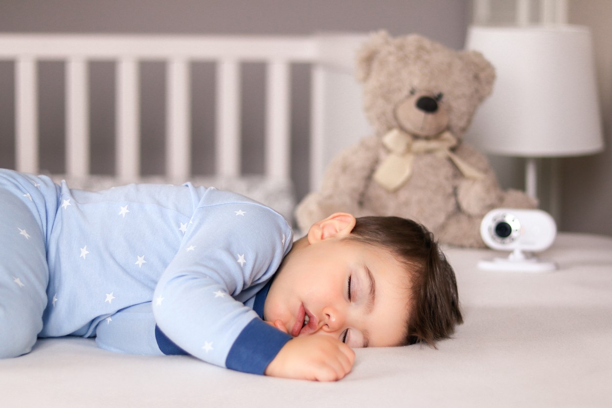 baby boy sleeping peacefully in crib at home with baby monitor camera in the background