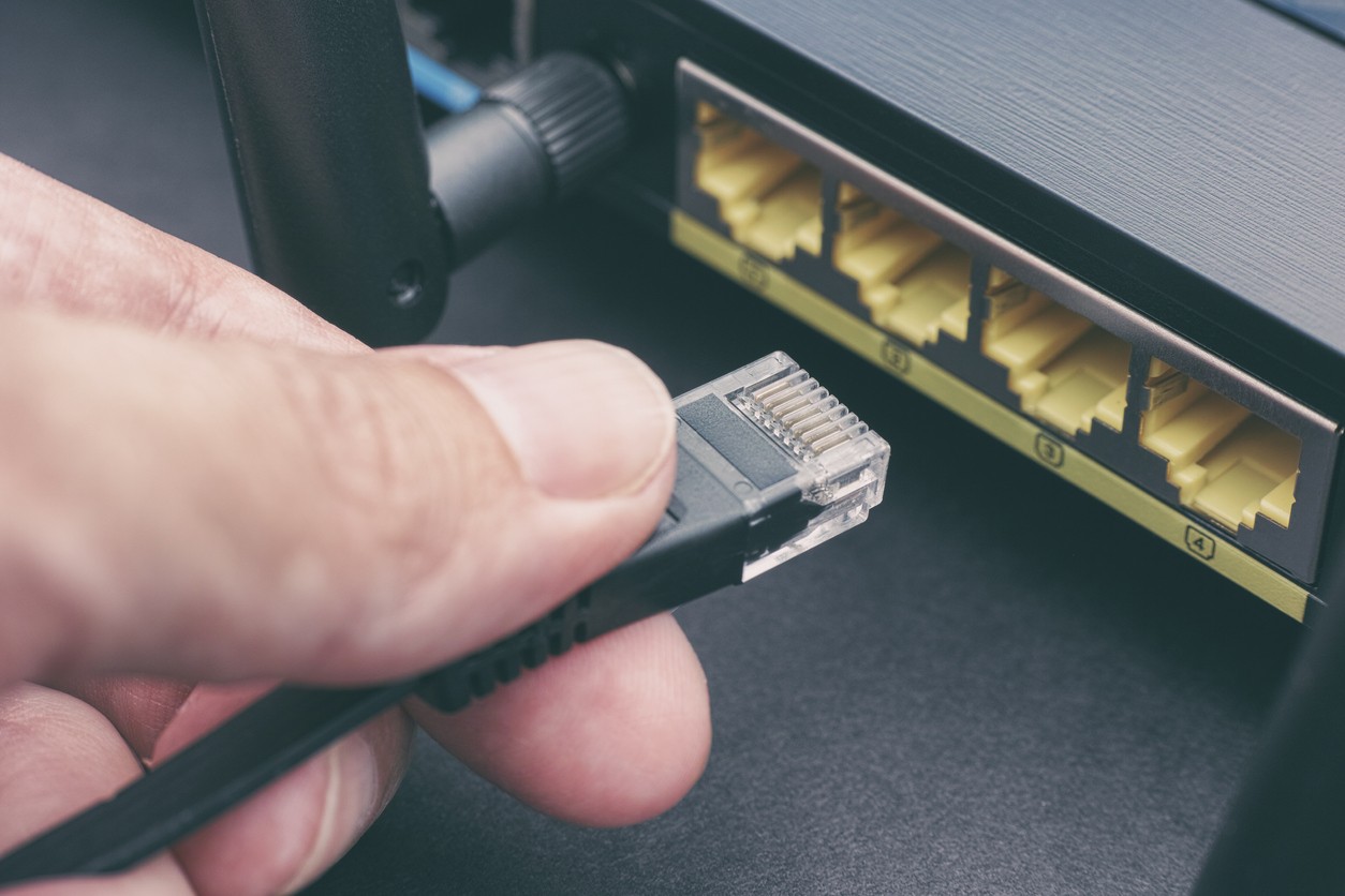 person plugging in ethernet cable to wireless internet router