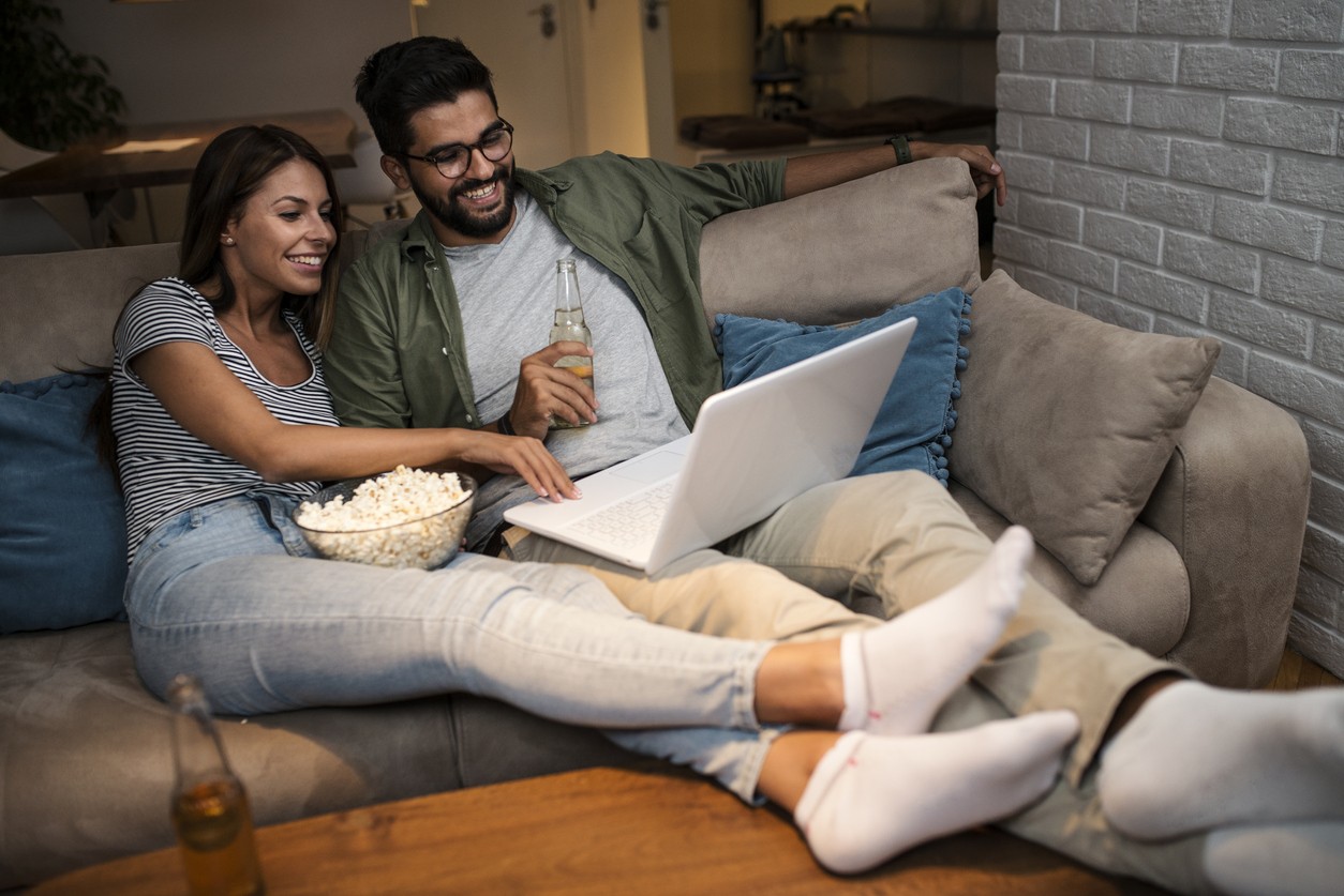 couple is lounging on the sofa and watching movies on a laptop