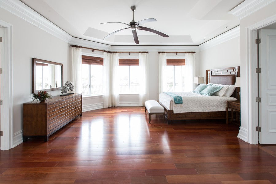 large bedroom with a ceiling fan, dresser, and bed in front of three windows with partially raised shades